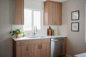 Kitchen with backsplash, stainless steel dishwasher, light stone countertops, and light brown cabinetry