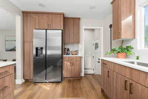 Kitchen with stainless steel fridge with ice dispenser, light wood finished floors, brown cabinets, and decorative backsplash