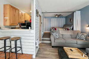 Living room with light wood-style floors, ceiling fan, wooden walls, and a textured ceiling