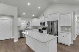 Kitchen with white cabinets, stainless steel appliances, light wood-type flooring, a kitchen island, and light stone counters