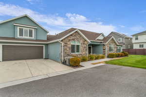 View of front of home featuring stone siding, concrete driveway, stucco siding, an attached garage, and roof with shingles