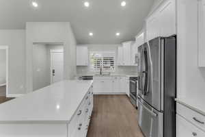 Kitchen with stainless steel appliances, light wood-type flooring, light stone countertops, white cabinetry, and recessed lighting