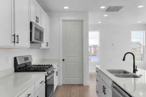 Kitchen with appliances with stainless steel finishes, white cabinets, recessed lighting, light wood finished floors, and light stone countertops