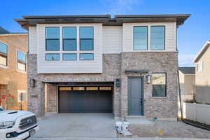 Contemporary home with concrete driveway, brick siding, and an attached garage