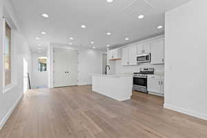 Kitchen featuring stainless steel appliances, white cabinetry, recessed lighting, light countertops, and an island with sink