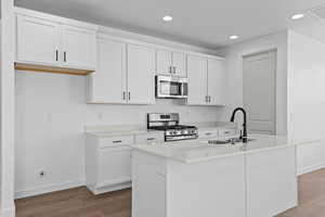 Kitchen with stainless steel appliances, white cabinetry, recessed lighting, a center island with sink, and dark wood-style floors