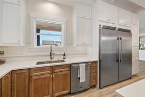 Kitchen with stainless steel appliances, white cabinetry, brown cabinetry, light stone counters, and light wood-style flooring