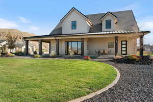 Back of house with stucco siding, a porch, a standing seam roof, and a yard