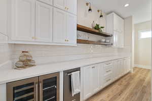 Bar area with wine cooler, white cabinetry, open shelves, light wood-style flooring, and backsplash