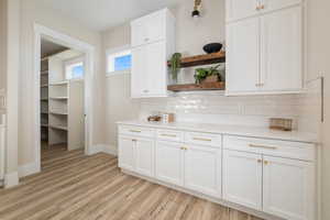 Kitchen featuring open shelves, white cabinets, light wood-type flooring, and backsplash