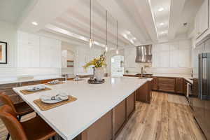 Kitchen featuring decorative backsplash, beam ceiling, white cabinetry, hanging light fixtures, and a kitchen bar