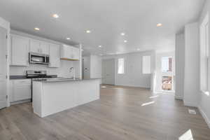 Kitchen with white cabinets, appliances with stainless steel finishes, recessed lighting, a kitchen island with sink, and light wood-style floors