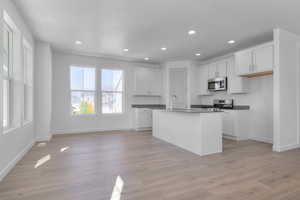 Kitchen featuring dark countertops, white cabinetry, recessed lighting, appliances with stainless steel finishes, and a center island with sink