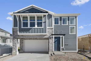View of front of house with board and batten siding, stone siding, an attached garage, and driveway