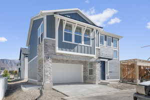 View of front facade featuring stone siding, board and batten siding, driveway, an attached garage, and a balcony