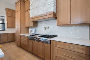 Kitchen with decorative backsplash, premium range hood, stainless steel gas stovetop, light wood-type flooring, and light stone counters