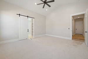 Unfurnished bedroom featuring a barn door, a walk in closet, recessed lighting, light colored carpet, and ceiling fan