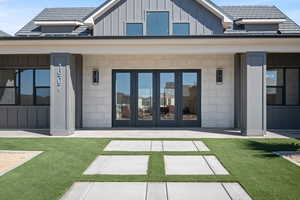 Rear view of house with board and batten siding, a porch, french doors, and a lawn