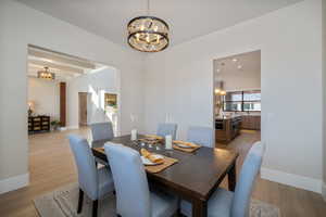 Dining space with a chandelier, light wood-type flooring, beamed ceiling, and recessed lighting