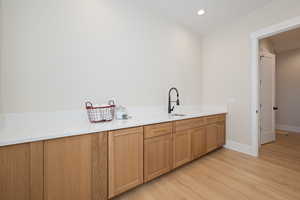 Bar featuring light wood finished floors, recessed lighting, light stone counters, and brown cabinetry