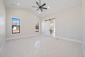Unfurnished bedroom featuring a barn door, light colored carpet, a ceiling fan, high vaulted ceiling, and ensuite bath