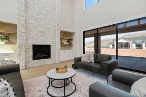 Living area featuring light wood-style flooring, a stone fireplace, a high ceiling, and a mountain view