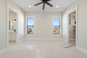 Unfurnished bedroom featuring a spacious closet, light carpet, recessed lighting, ceiling fan, and ensuite bath