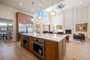 Kitchen featuring brown cabinetry, light wood-style floors, a fireplace, hanging light fixtures, and a high ceiling