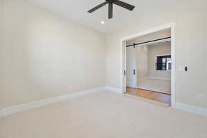 Unfurnished bedroom featuring carpet, a barn door, recessed lighting, and ceiling fan