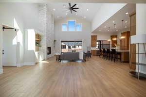 Living area with recessed lighting, light wood-style flooring, a ceiling fan, a stone fireplace, and high vaulted ceiling