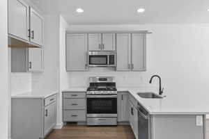 Kitchen featuring a textured ceiling, stainless steel appliances, gray cabinetry, light stone counters, and a peninsula