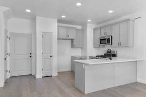 Kitchen with gray cabinetry, a peninsula, recessed lighting, tasteful backsplash, and light wood-style floors