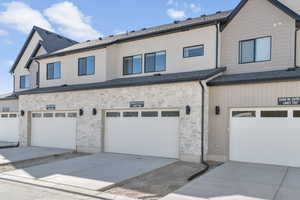 Back of property featuring stone siding, concrete driveway, and roof with shingles