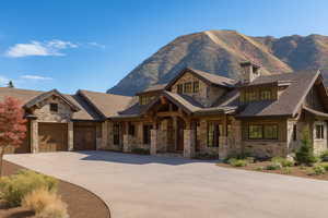 View of front of house with stone siding, driveway, a mountain view, a chimney, and an attached garage