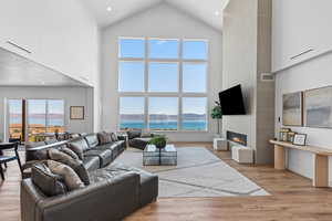 Living room with a water view, light wood-style floors, a fireplace, high vaulted ceiling, and recessed lighting