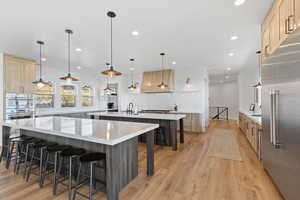 Kitchen with light brown cabinetry, light stone countertops, a breakfast bar area, appliances with stainless steel finishes, and recessed lighting
