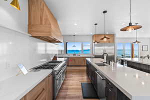 Kitchen with light stone counters, hanging light fixtures, high quality appliances, light wood-style floors, and custom range hood