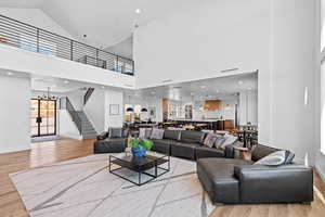 Living area featuring light wood-style floors, high vaulted ceiling, stairs, recessed lighting, and a chandelier