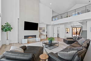 Living area featuring a tiled fireplace, high vaulted ceiling, wood finished floors, stairway, and recessed lighting