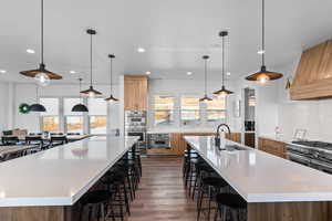 Kitchen with a kitchen bar, pendant lighting, light stone counters, light wood-type flooring, and brown cabinets