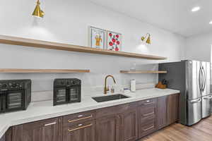 Kitchen featuring open shelves, dark brown cabinetry, freestanding refrigerator, light wood-type flooring, and recessed lighting