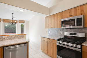 Kitchen featuring appliances with stainless steel finishes, light stone counters, light tile patterned flooring, backsplash, and hanging light fixtures