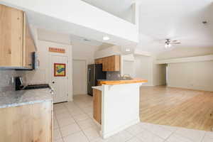 Kitchen with decorative backsplash, light tile patterned floors, vaulted ceiling, appliances with stainless steel finishes, and ceiling fan