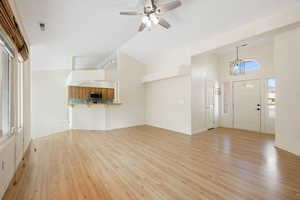 Unfurnished living room featuring light wood-style flooring, a ceiling fan, and high vaulted ceiling