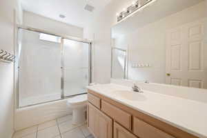 Full bathroom with enclosed tub / shower combo, vanity, and light tile patterned flooring