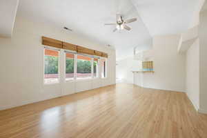 Unfurnished living room featuring light wood-style floors, a ceiling fan, and lofted ceiling