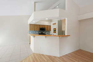 Kitchen featuring a breakfast bar area, brown cabinets, backsplash, light wood finished floors, and appliances with stainless steel finishes