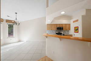Kitchen featuring butcher block counters, a breakfast bar area, backsplash, light tile patterned flooring, and decorative light fixtures