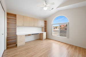 Unfurnished office with built in study area, lofted ceiling, light wood-style flooring, and ceiling fan