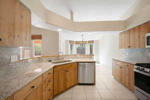 Kitchen with backsplash, appliances with stainless steel finishes, a peninsula, light tile patterned flooring, and a chandelier